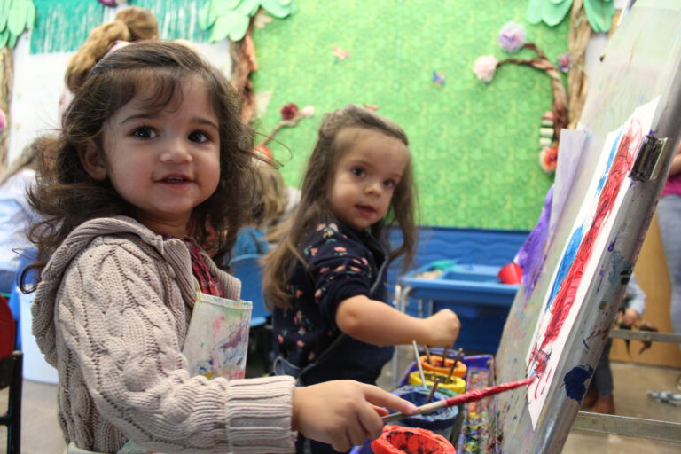 Photo of two children wearing smocks and painting with brushes and easels