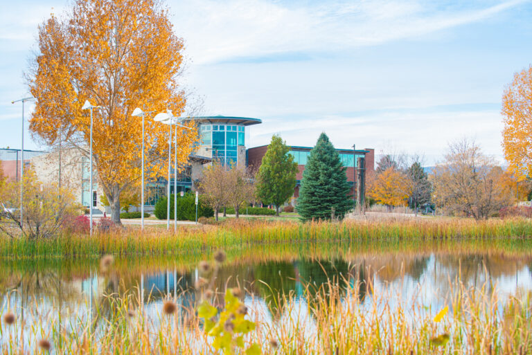 Photo of the Longmont Museum building exterior, as viewed from across a reflective pond and surrounded by autumn trees and grass